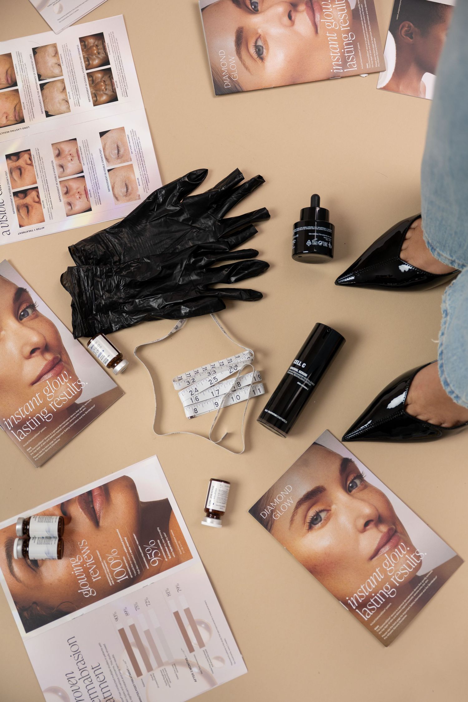 Beauty tools flatlay with black gloves, serum bottles, measuring tape, and cosmetic brochures on beige background.