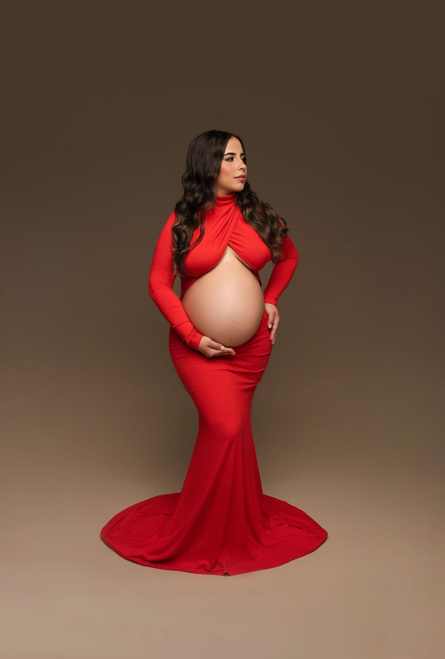 A woman in a flowing red dress poses gracefully in a series of maternity photos against a neutral studio backdrop.