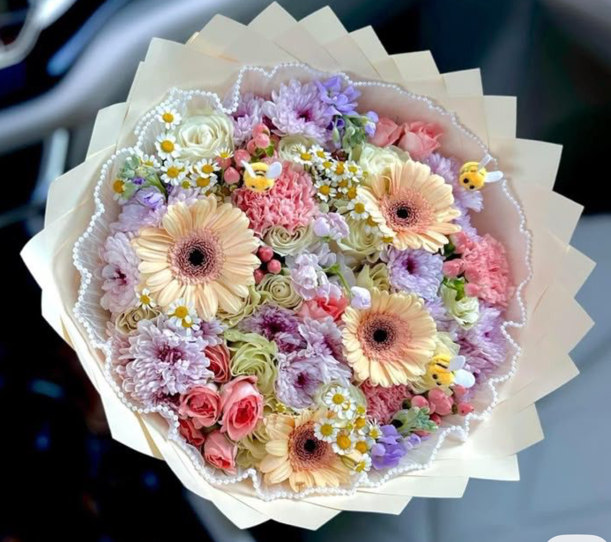 Lush pastel flower bouquet with gerbera daisies, roses, carnations, and chamomile in cream wrapping.