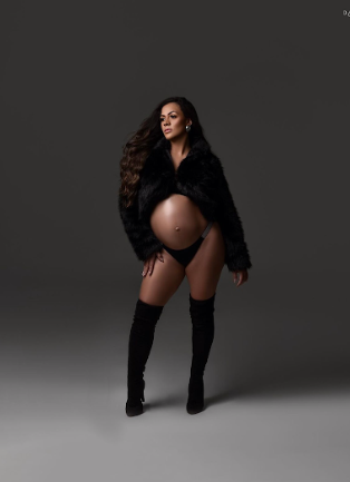 A maternity photoshoot featuring a model in a black fur coat and thigh-high boots against a dark background.