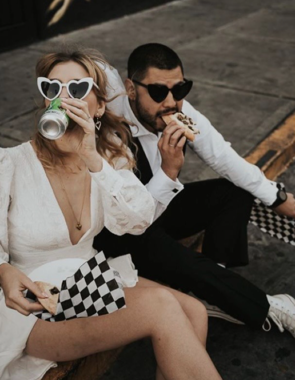 Couple in white outfits posing with checkered racing flag and sunglasses in vintage-inspired racing photoshoot.