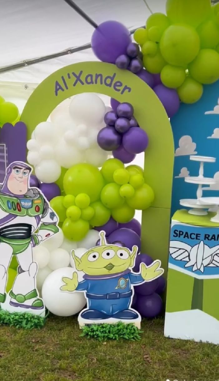 Toy Story themed party decoration with green and purple balloon arch featuring Buzz Lightyear and alien cutouts.