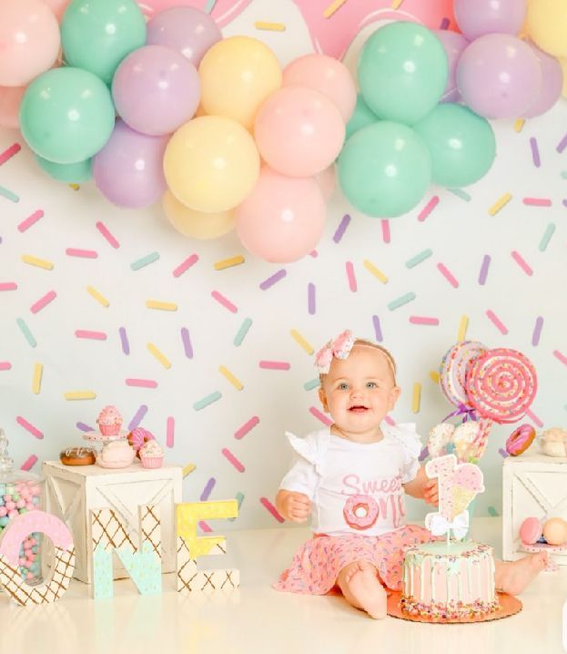 Pastel balloon arch and sprinkle decorations create a festive backdrop for a pink and white birthday cake celebration.