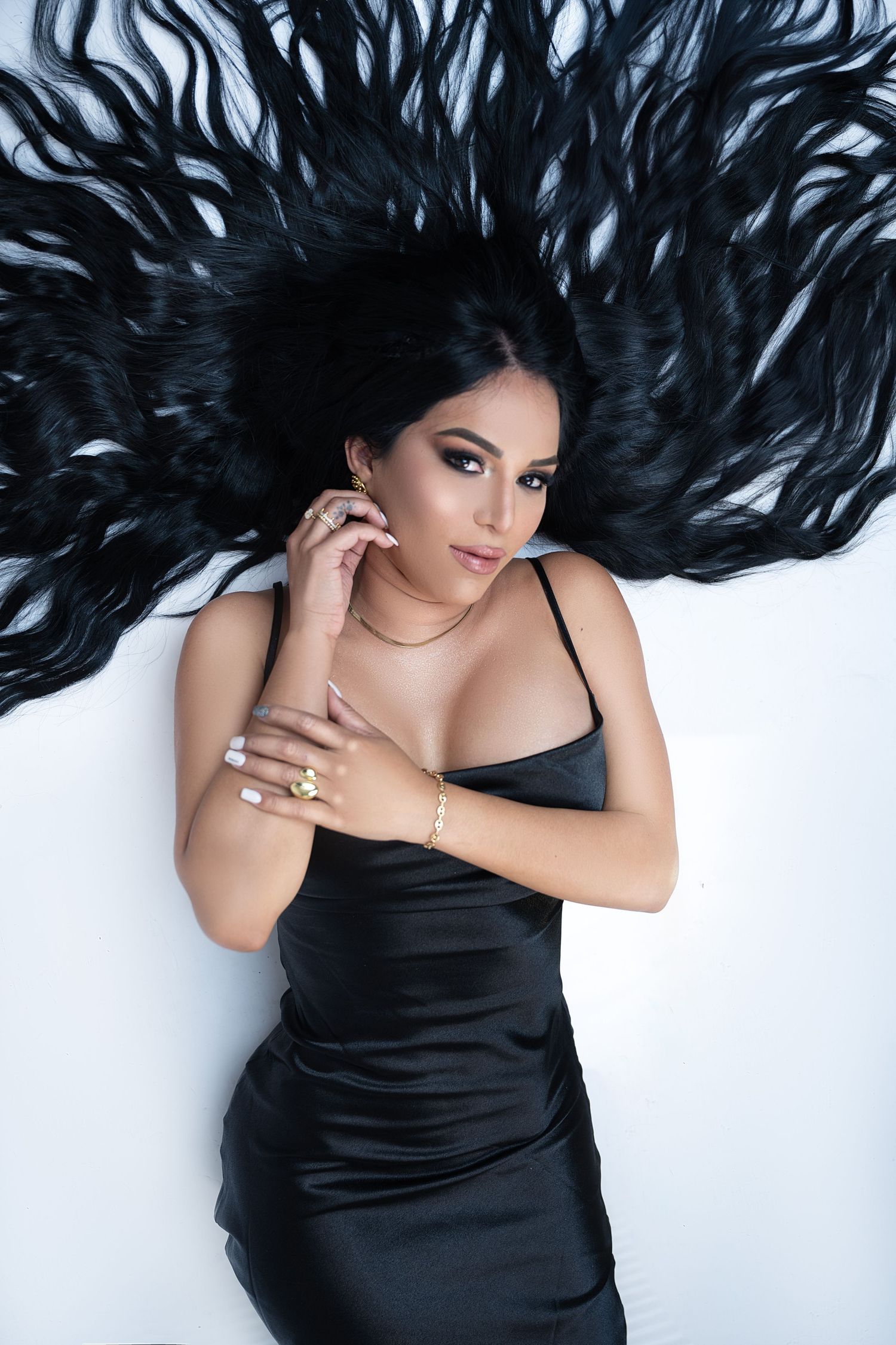 Dramatic overhead shot with long black hair fanned out against white background in black satin dress.