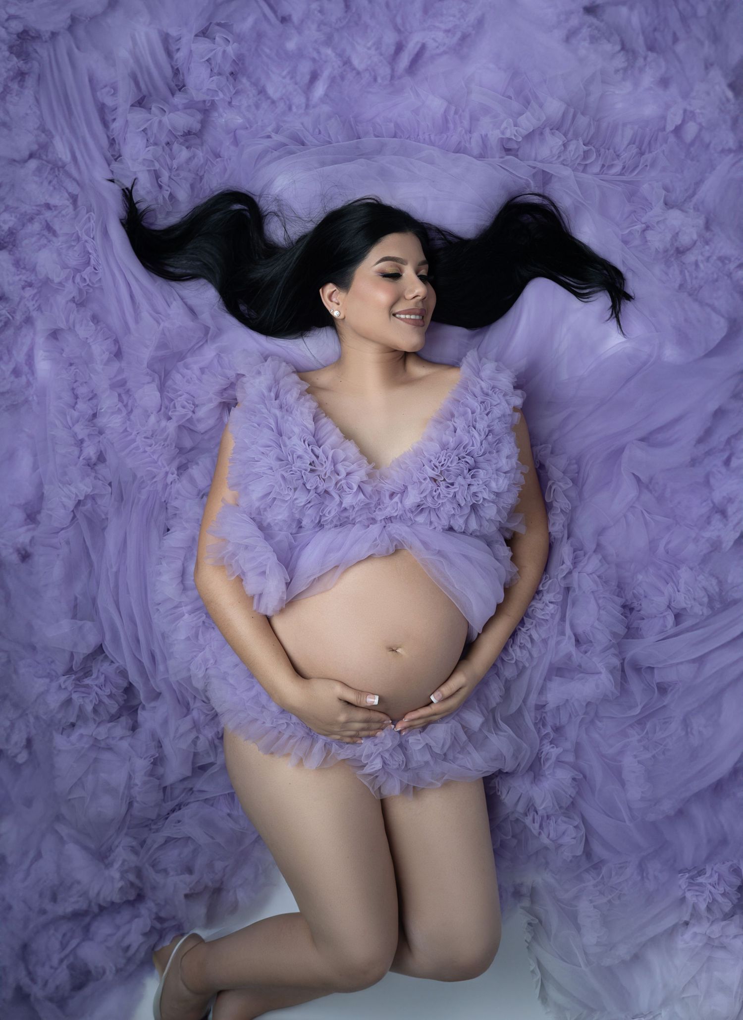 Maternity portrait with purple tulle fabric and flowing dark hair against matching purple background.