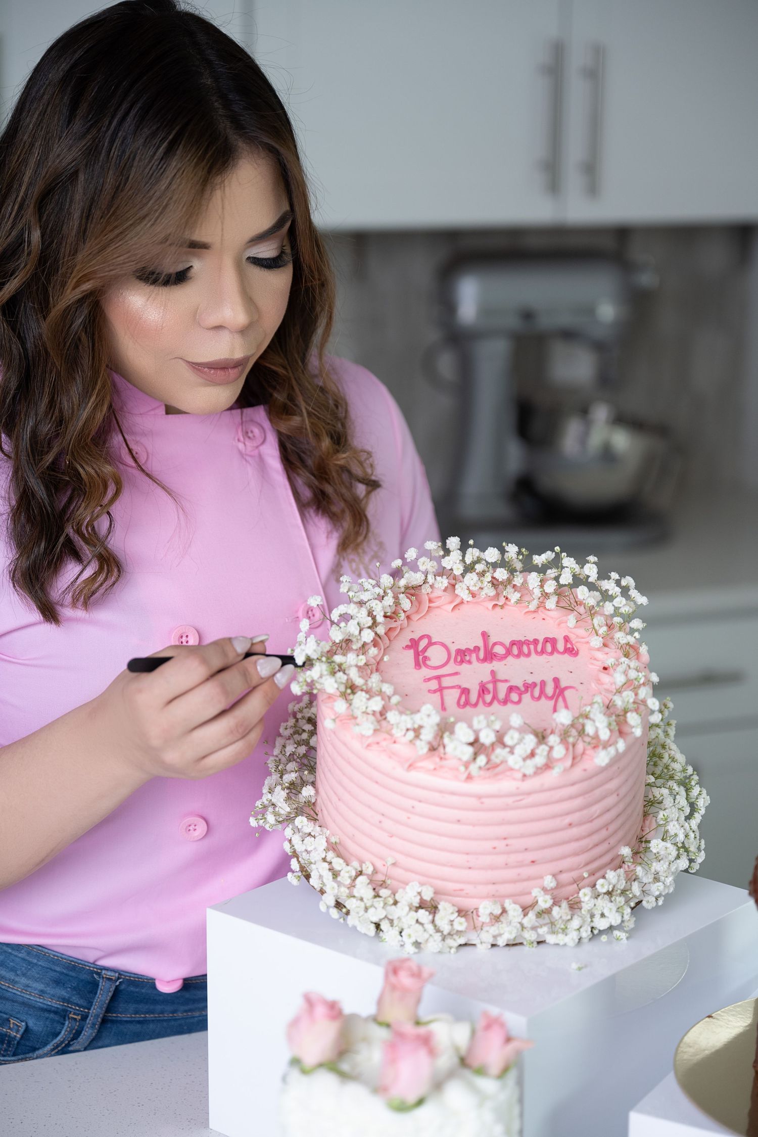 Pink celebration cake decorated with baby's breath flowers being prepared in modern kitchen.