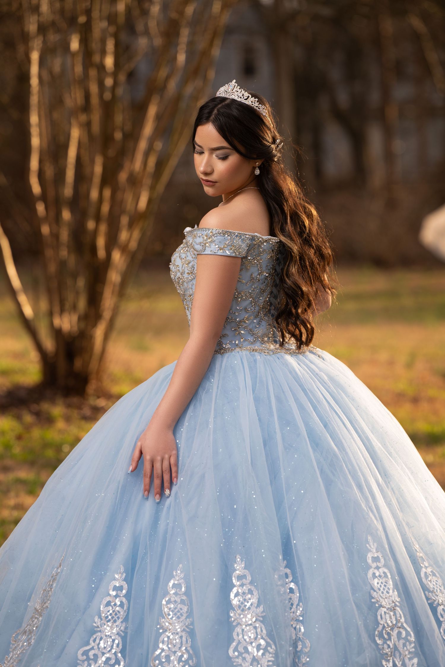 An elegant powder blue quinceañera ball gown with silver embellishments sparkles in golden sunset lighting.