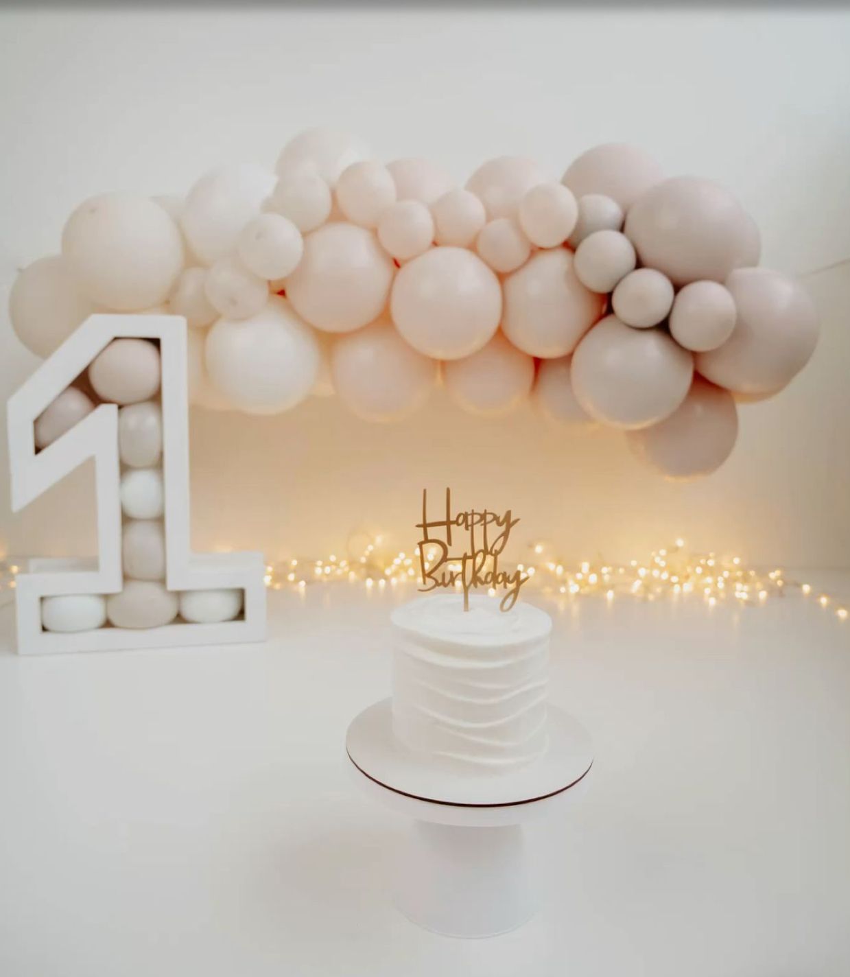 White balloon arch decorations with twinkling fairy lights create an elegant party atmosphere against a neutral backdrop.