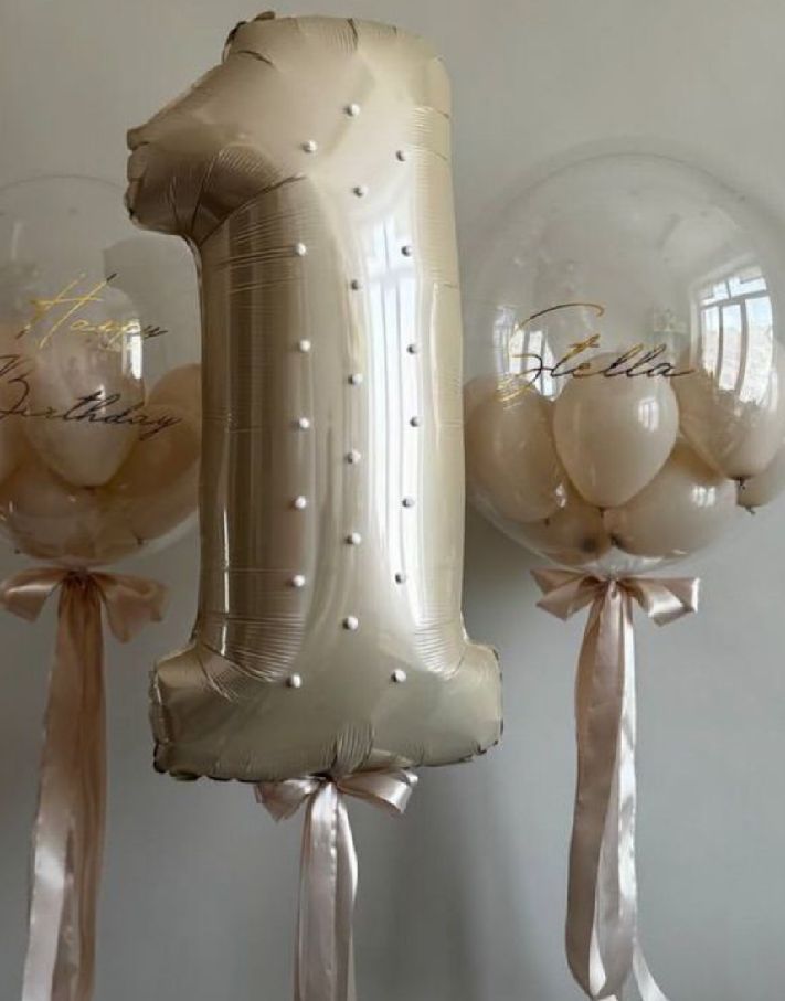 Gold number one balloon with clear balloons decorated with ribbons for a first birthday celebration.