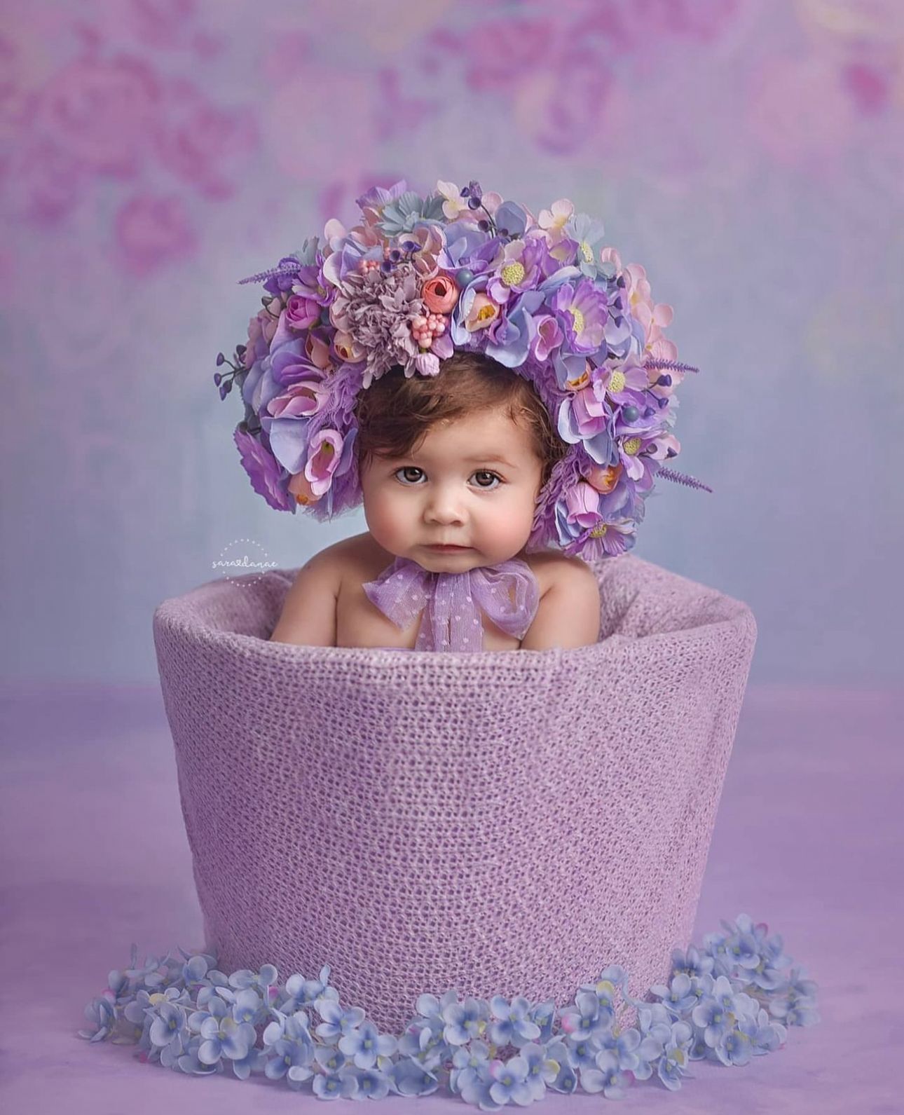 Sweet baby photography session in purple bowl with delicate floral decorations and soft pastel backdrop.