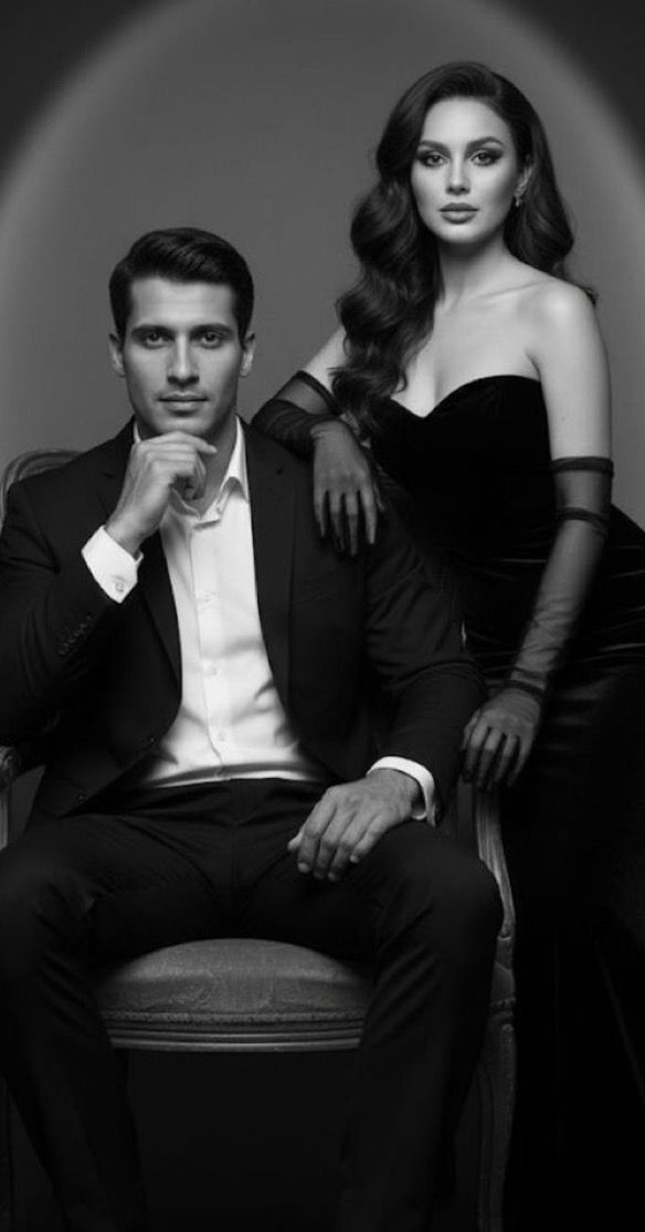Elegant black and white portrait of a man in a suit and woman in black gown posing together in a studio setting.