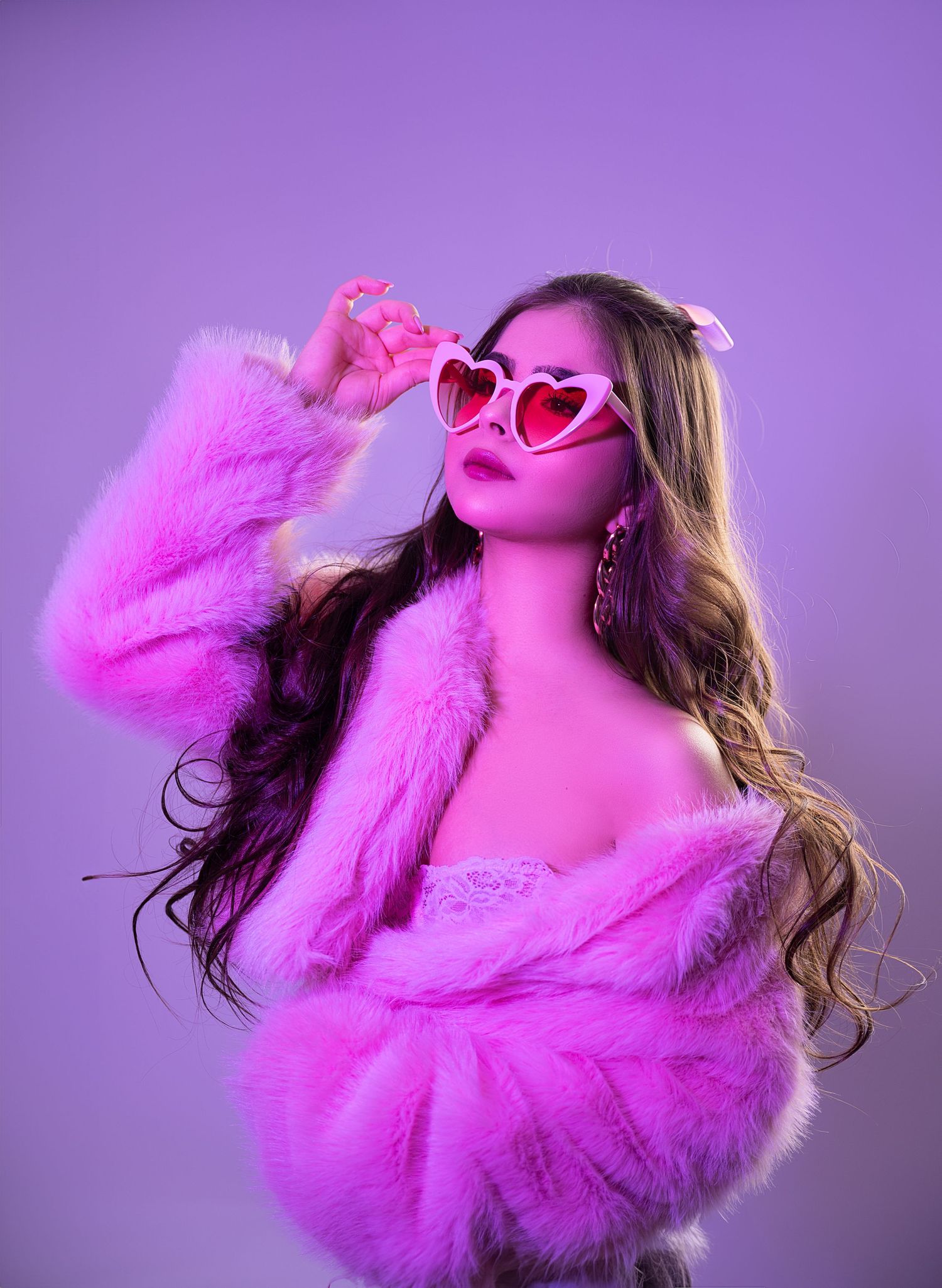 Fashion portrait with pink fur coat and heart shaped glasses against purple background.