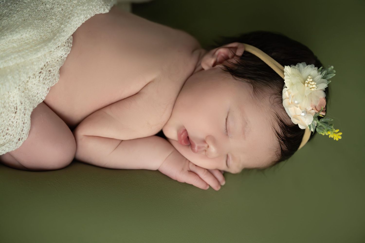 Sleeping newborn with floral headband resting on green fabric.