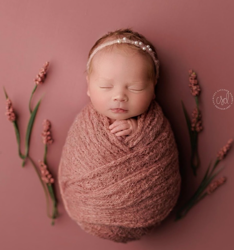 Newborn photography series in pink tones showing baby wrapped in soft fabric with delicate floral accents.