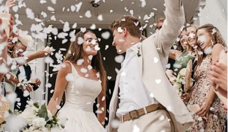 A joyful wedding celebration with white confetti falling as newlyweds walk through a crowd of cheering guests.