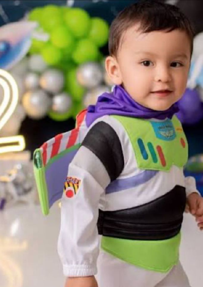 A small child wearing a Buzz Lightyear costume from Toy Story poses against a festive backdrop with balloons.