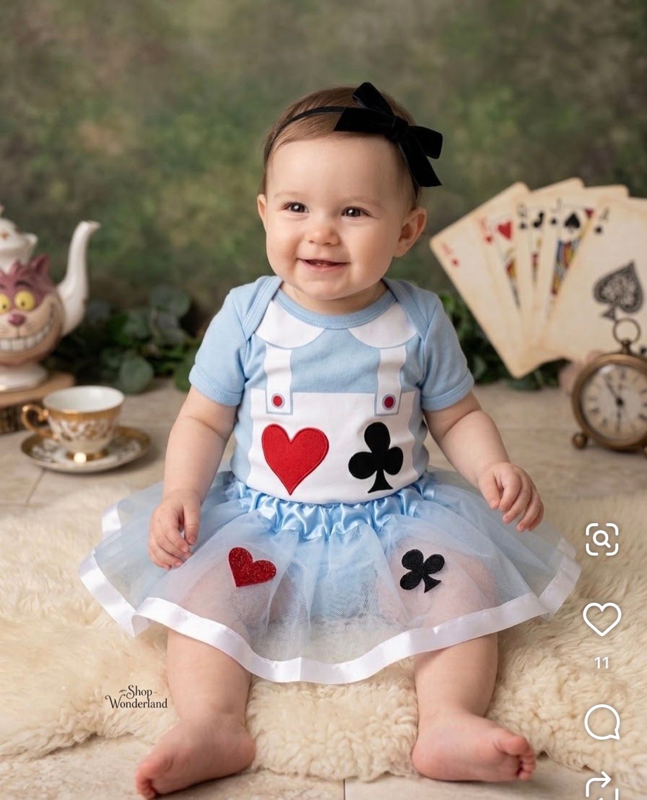 Baby girl in Alice in Wonderland costume with blue dress, tutu skirt, and playing card suit symbols at themed photo shoot.