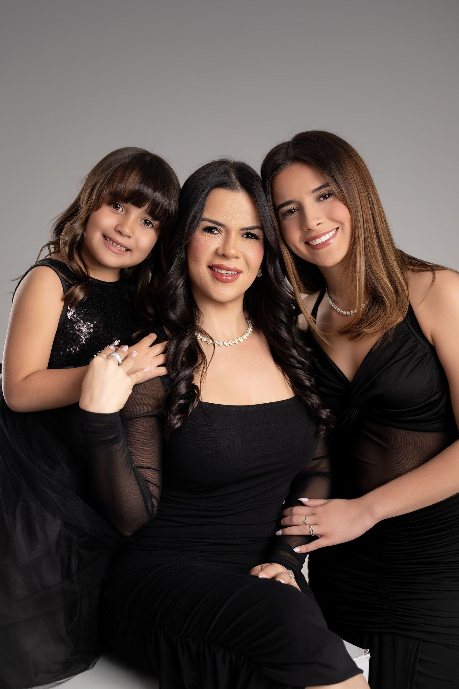 Three women in matching black dresses pose together for a elegant studio portrait photo.