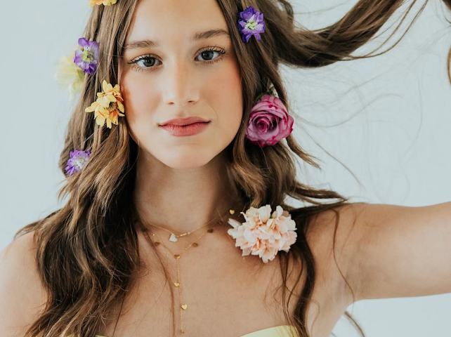 Young woman with flowers in long wavy hair wearing yellow top in soft floral beauty portrait.