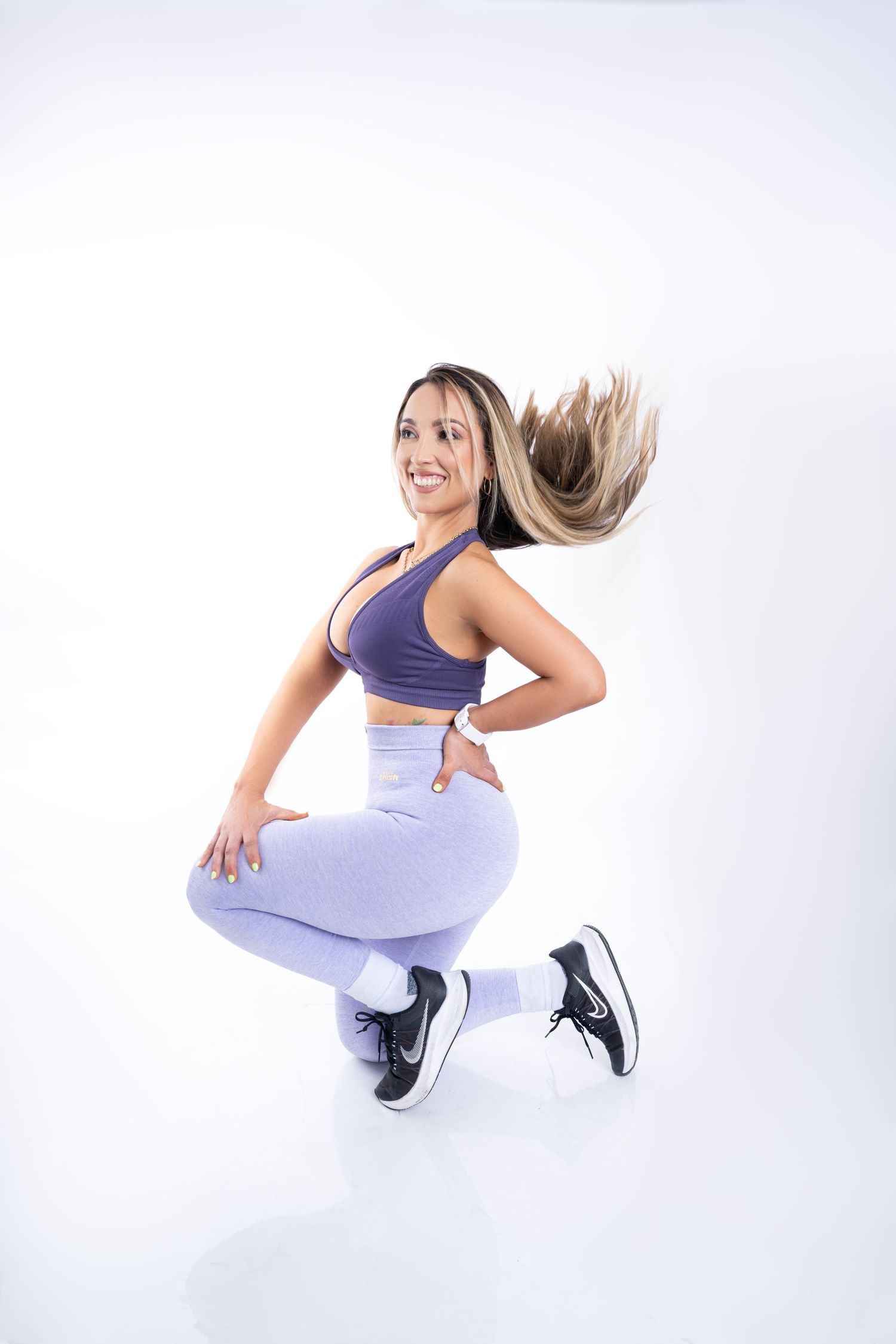 Fitness model in purple workout attire performing dynamic jumping pose on white background.