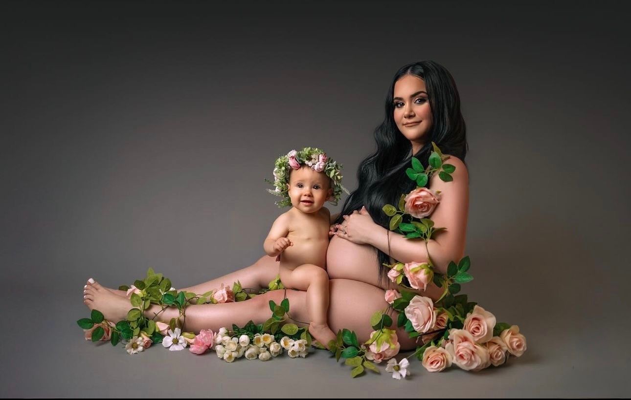 Mother and baby posed together with roses and greenery in a studio maternity and newborn photography session.