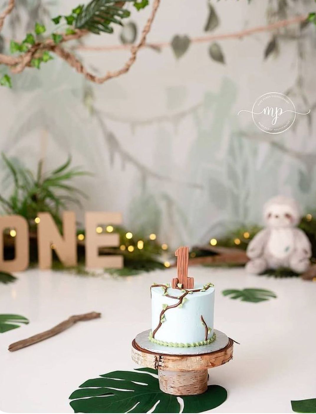 Elegant white and green birthday cake displayed on a rustic wooden stand with delicate decorative elements.