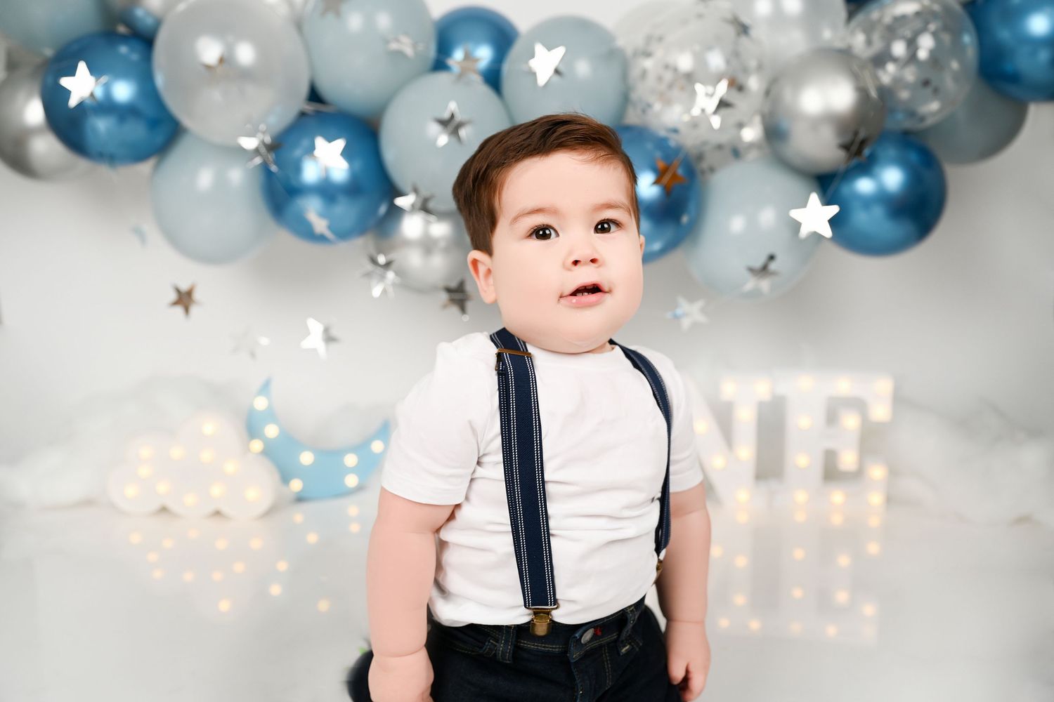 First birthday photo backdrop with blue and silver balloons and illuminated ONE sign.