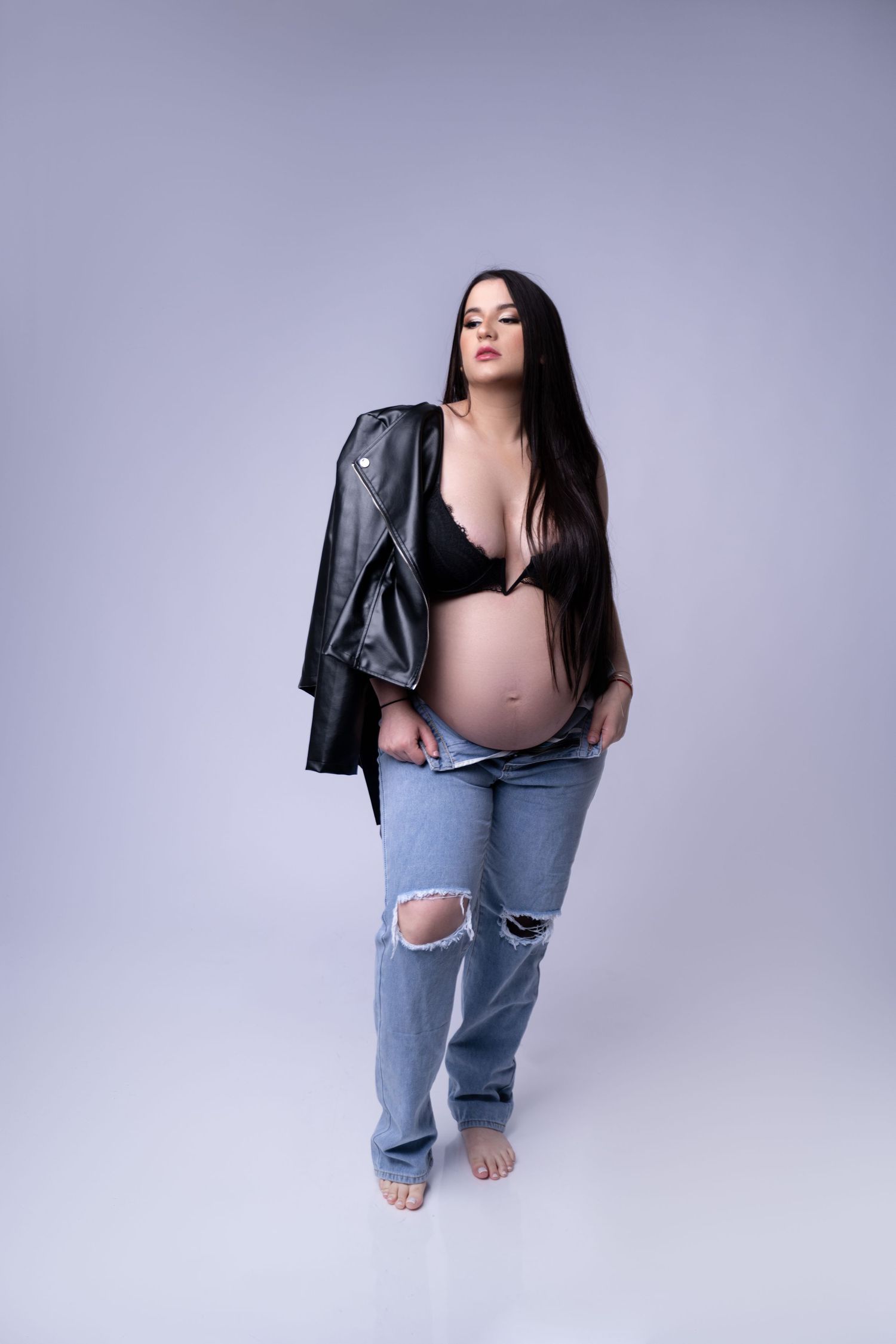 Artistic maternity pose in black lingerie and formal gloves against neutral background.