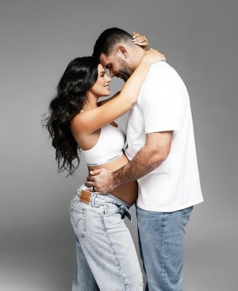 A couple in casual attire embracing and sharing an intimate moment against a gray studio background.