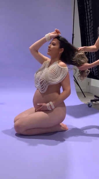 Figure poses gracefully in pearl necklaces against purple backdrop in artistic nude photography series.