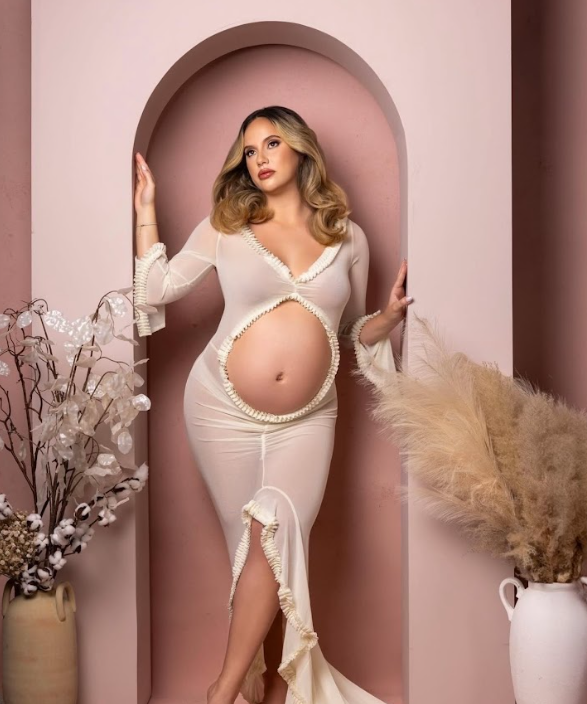 Maternity photo series showing an elegant woman in white dress against pink backdrop with dried pampas grass and floral decor.