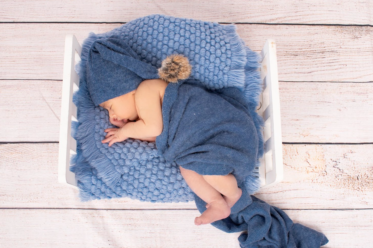 Sleeping newborn wrapped in soft blue knitted blanket on rustic wooden background.