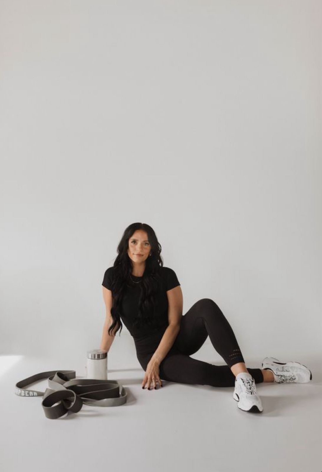 Woman in black athletic wear sitting on floor with resistance bands and water bottle for workout.