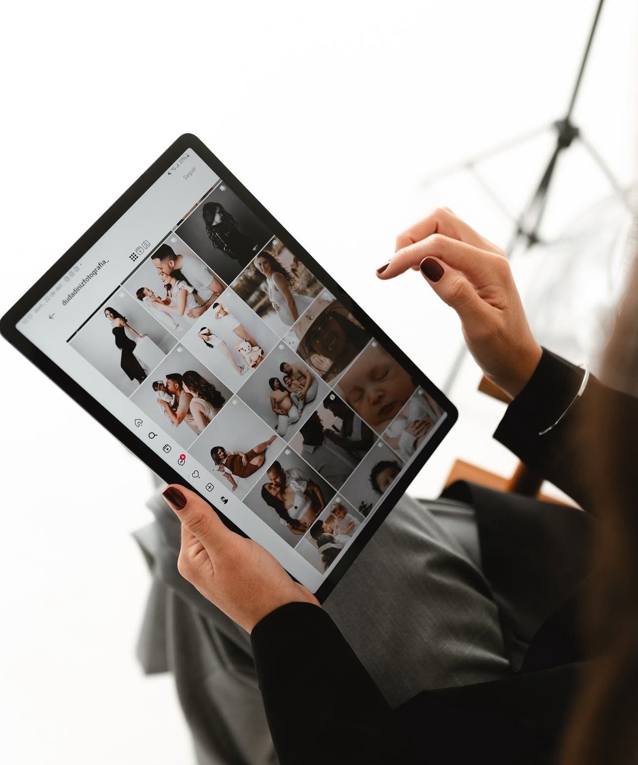 A woman holds a tablet displaying a grid of professional photos in a bright photography studio setting.