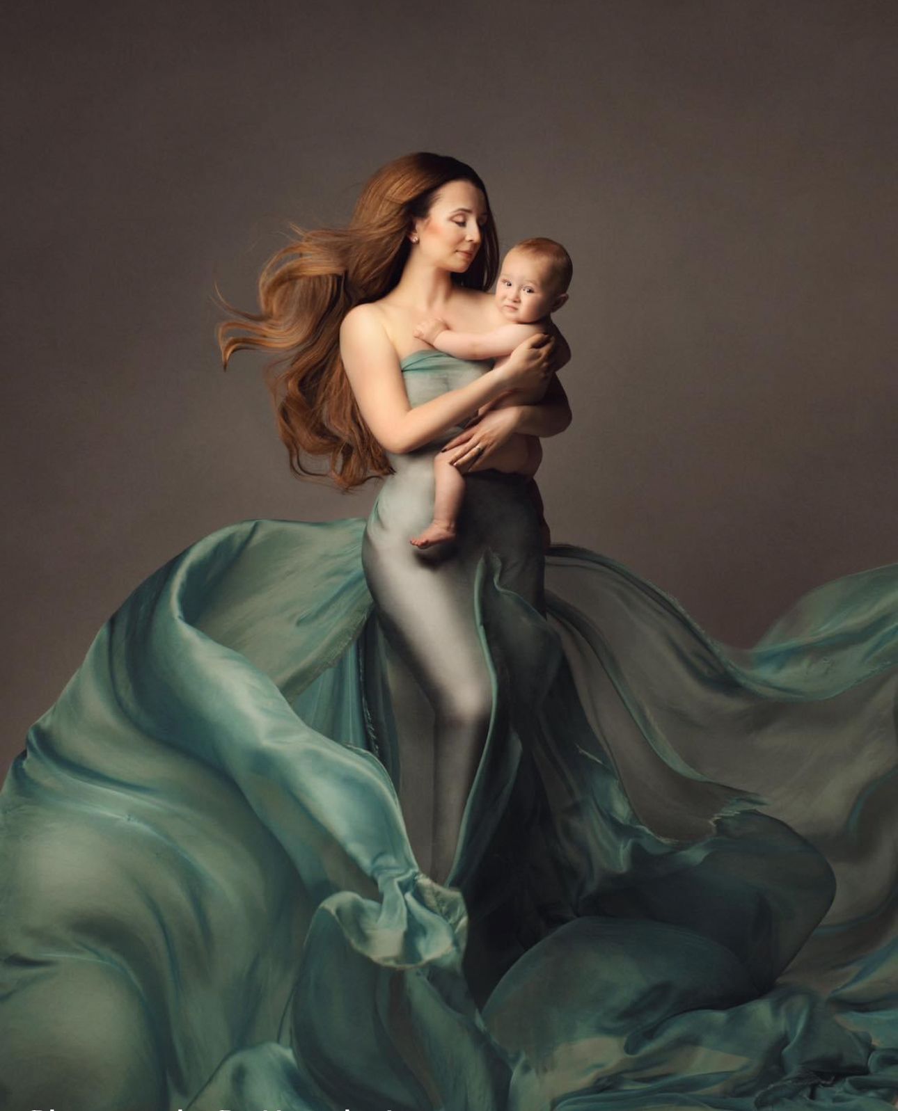 Mother in flowing teal fabric holds newborn baby in elegant fine art maternity portrait photography.