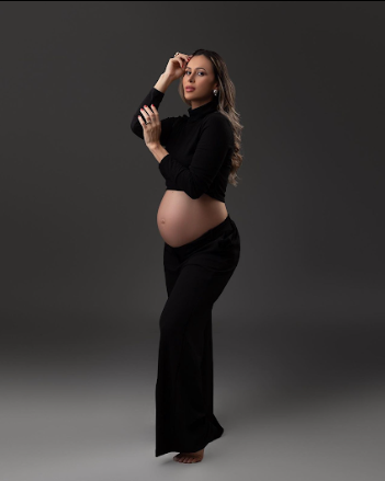 Elegant maternity photo featuring a woman in black attire posing gracefully against a dark backdrop.