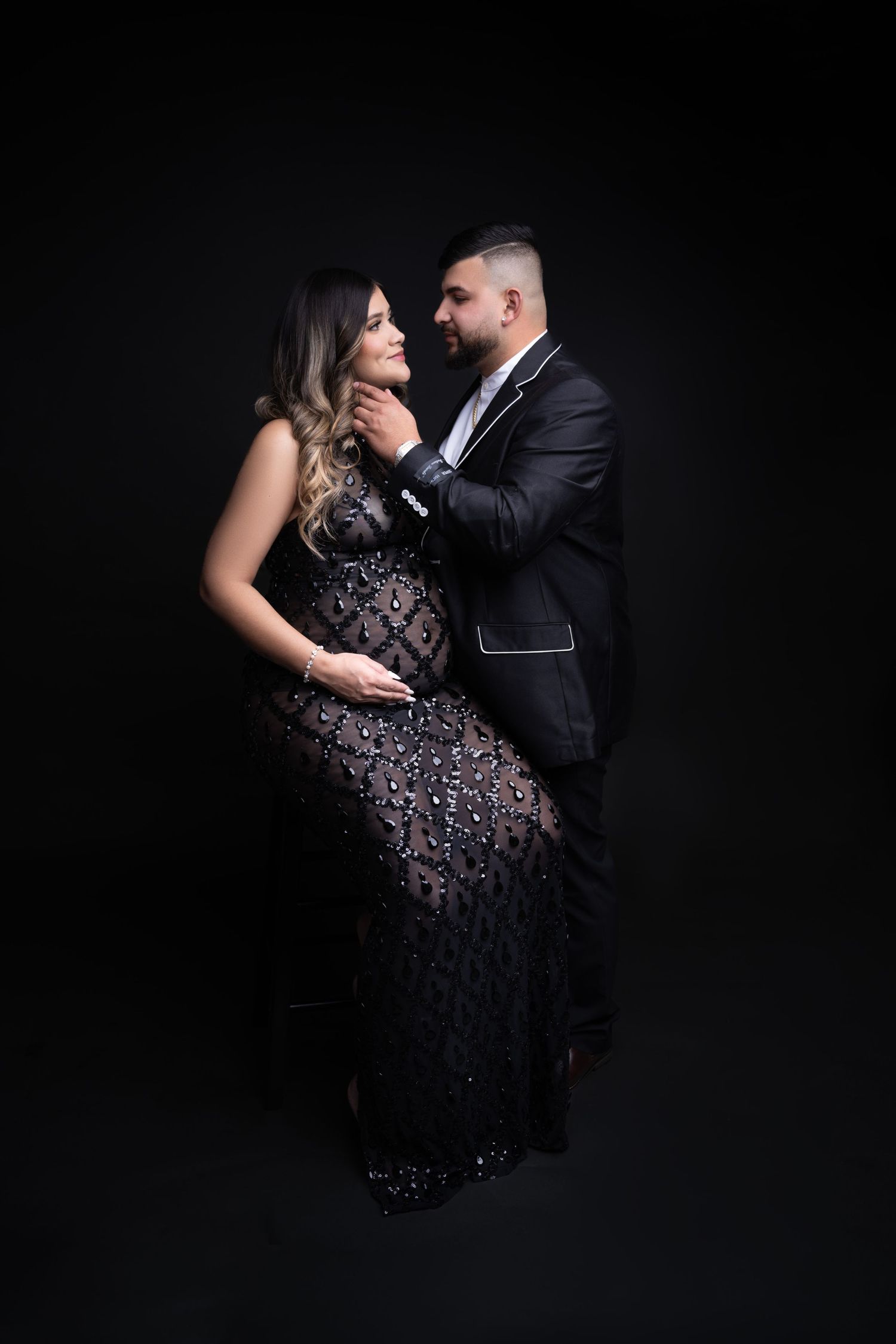 Intimate portrait of couple in formal wear embracing against dark background.