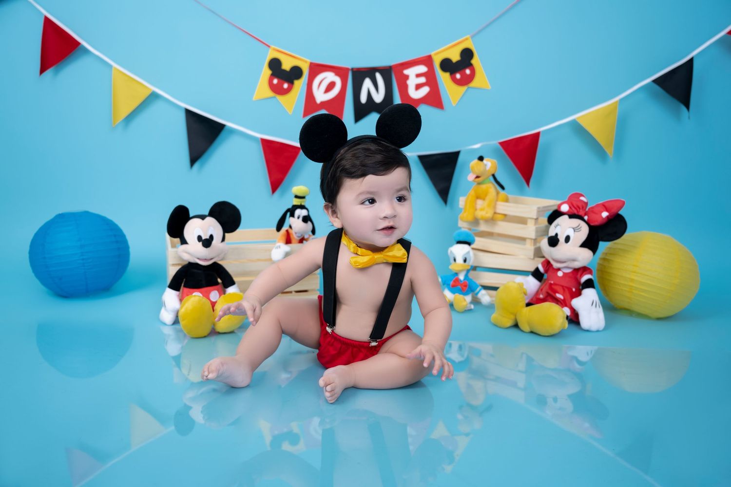 Festive Mickey Mouse themed setup with colorful banners and plush toys on blue background.