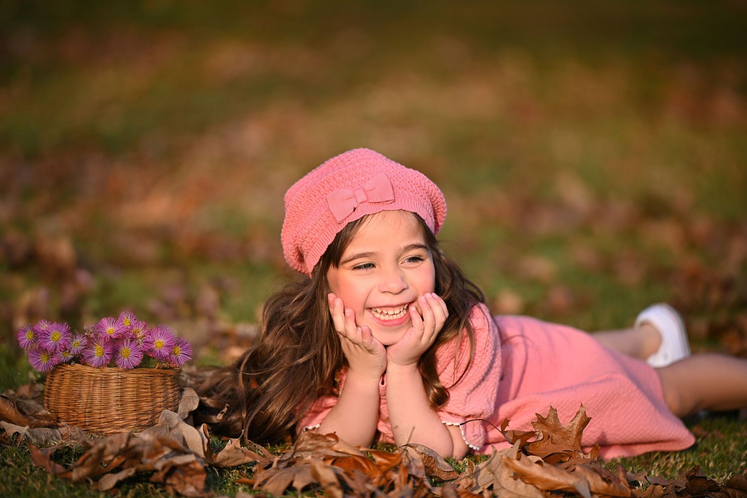 Autumn outdoor portrait with pink beret and basket of flowers among fallen leaves.