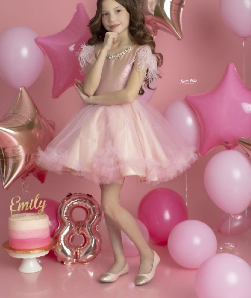 Pink birthday party scene with balloons, decorations and tulle dress against pink backdrop.