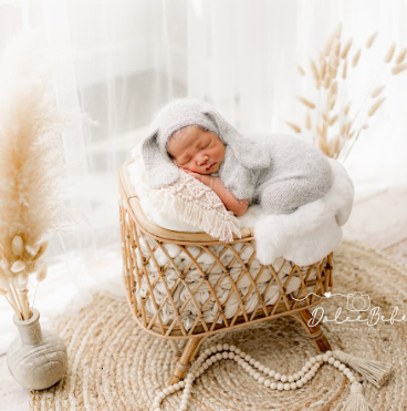 A peaceful newborn sleeping in a woven rattan basket surrounded by soft white fabrics and decorative pearls.