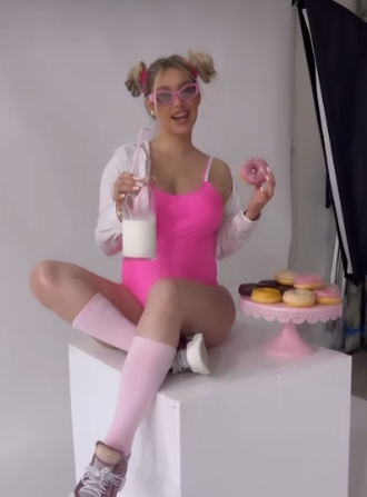 Person in pink and white outfit sitting on chair with donuts and milk enjoying a sweet treat and playful moment.