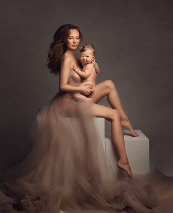 Mother and baby portrait session with soft tulle dress in dramatic studio lighting.