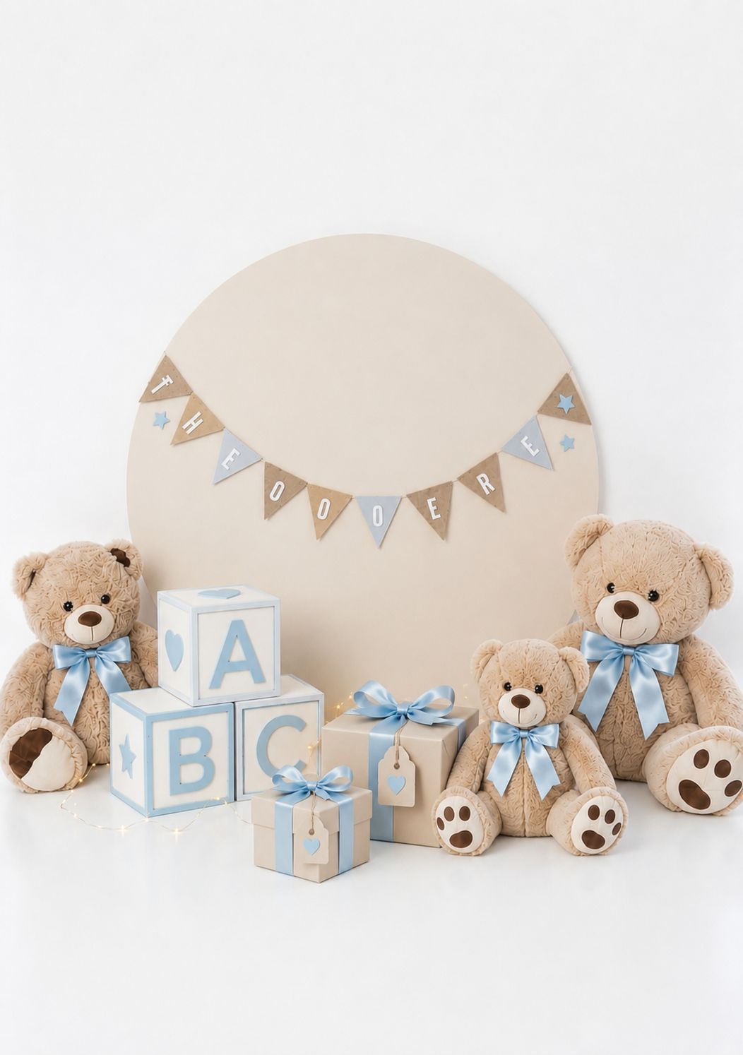 Three teddy bears with blue bows beside ABC blocks and gifts in front of a beige circle backdrop with bunting.