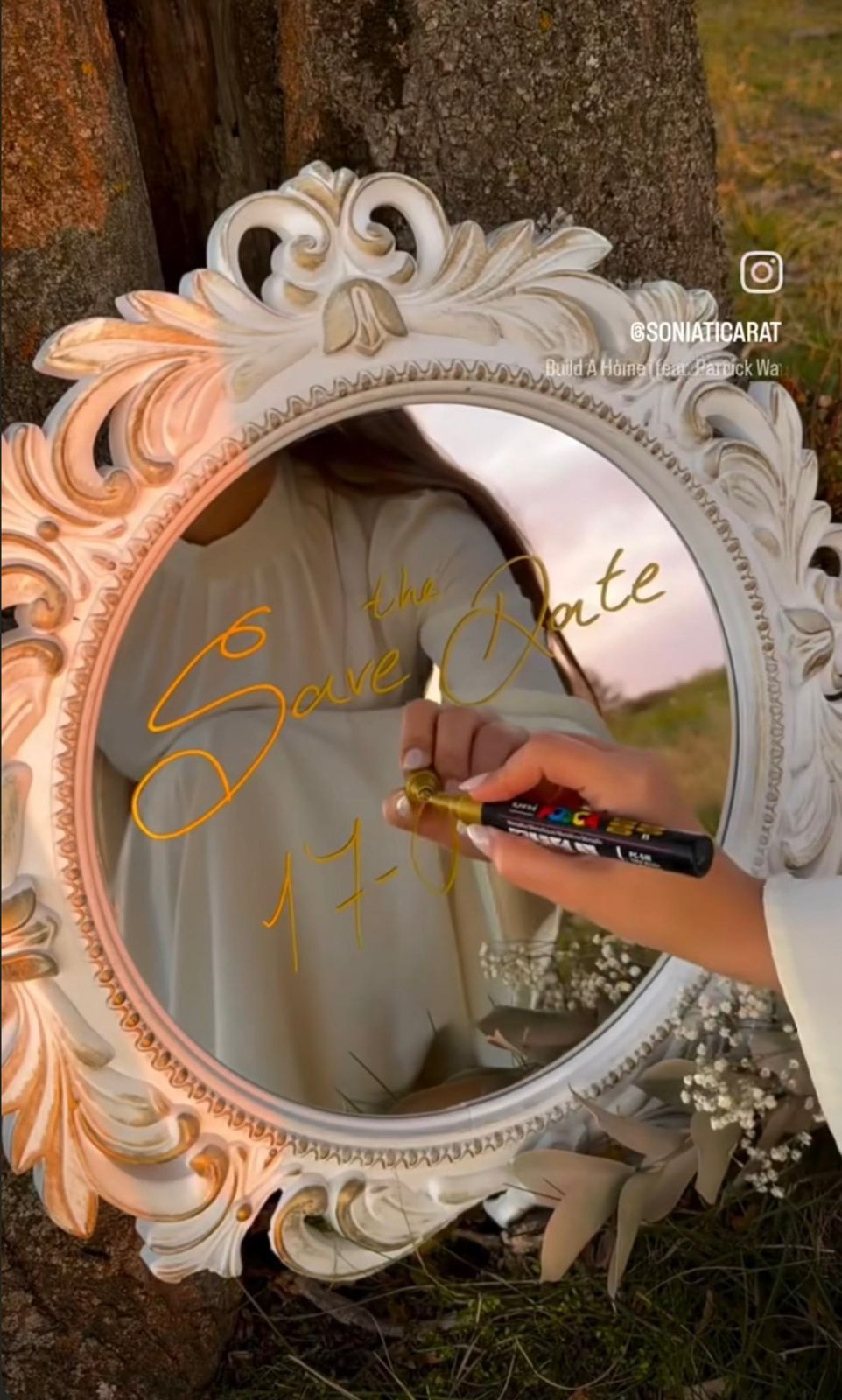 Ornate white vintage mirror with Save the Date written in gold marker leaning against a tree.