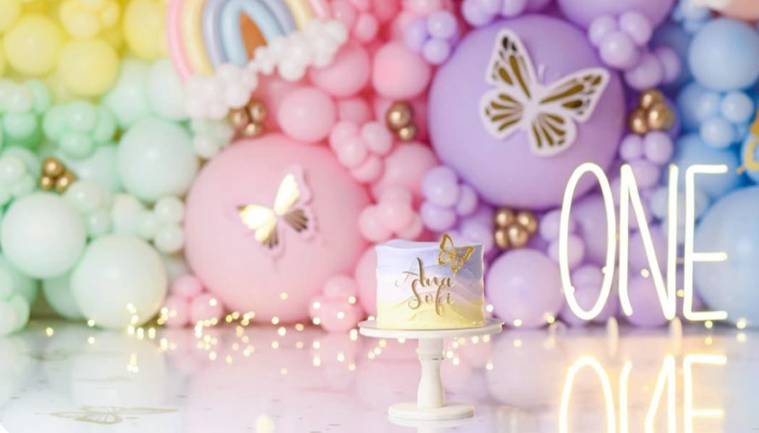 Colorful pastel balloon decorations with butterflies and floral accents create a dreamy party atmosphere.