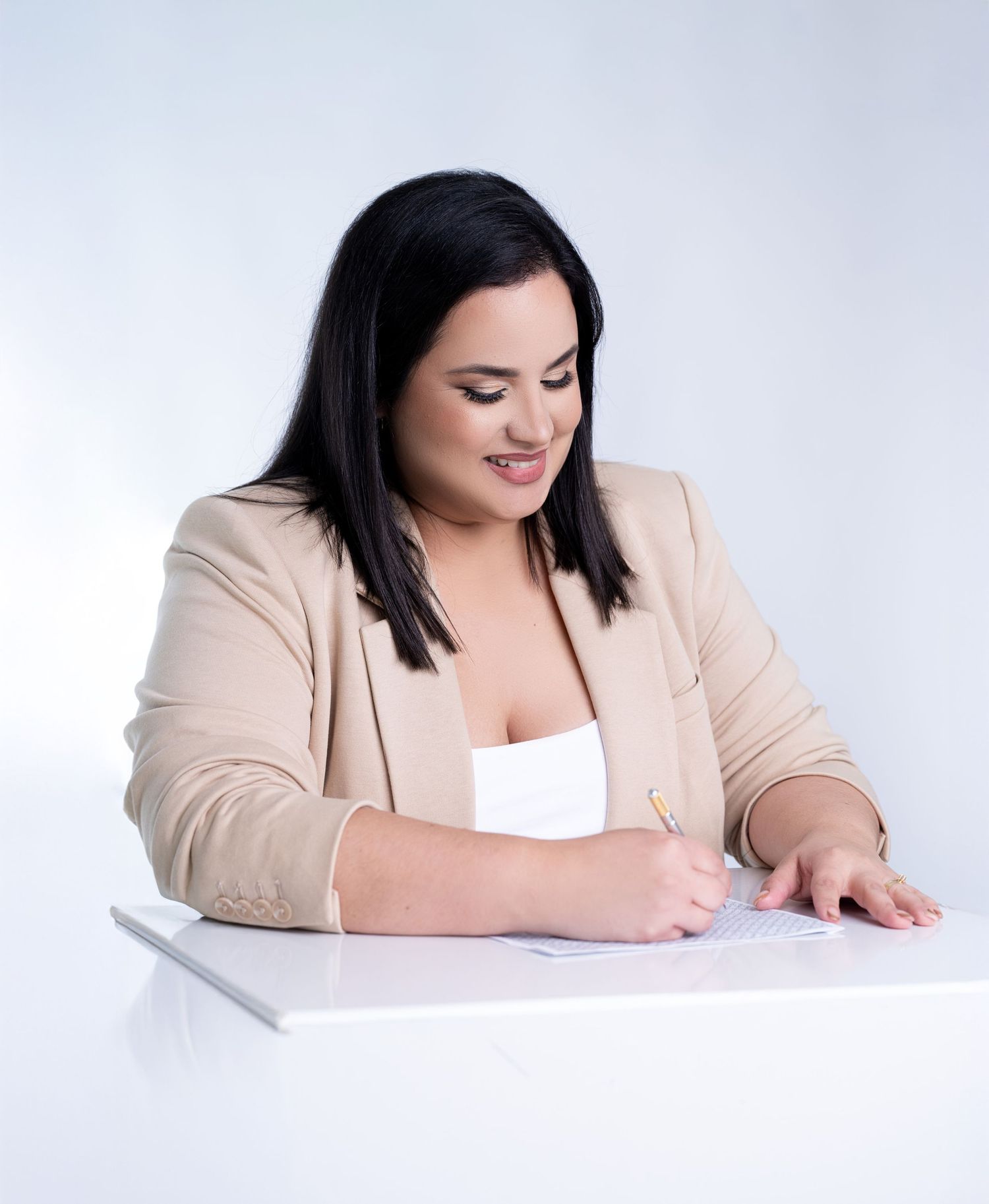 Professional writing on paper while wearing beige blazer at white desk.