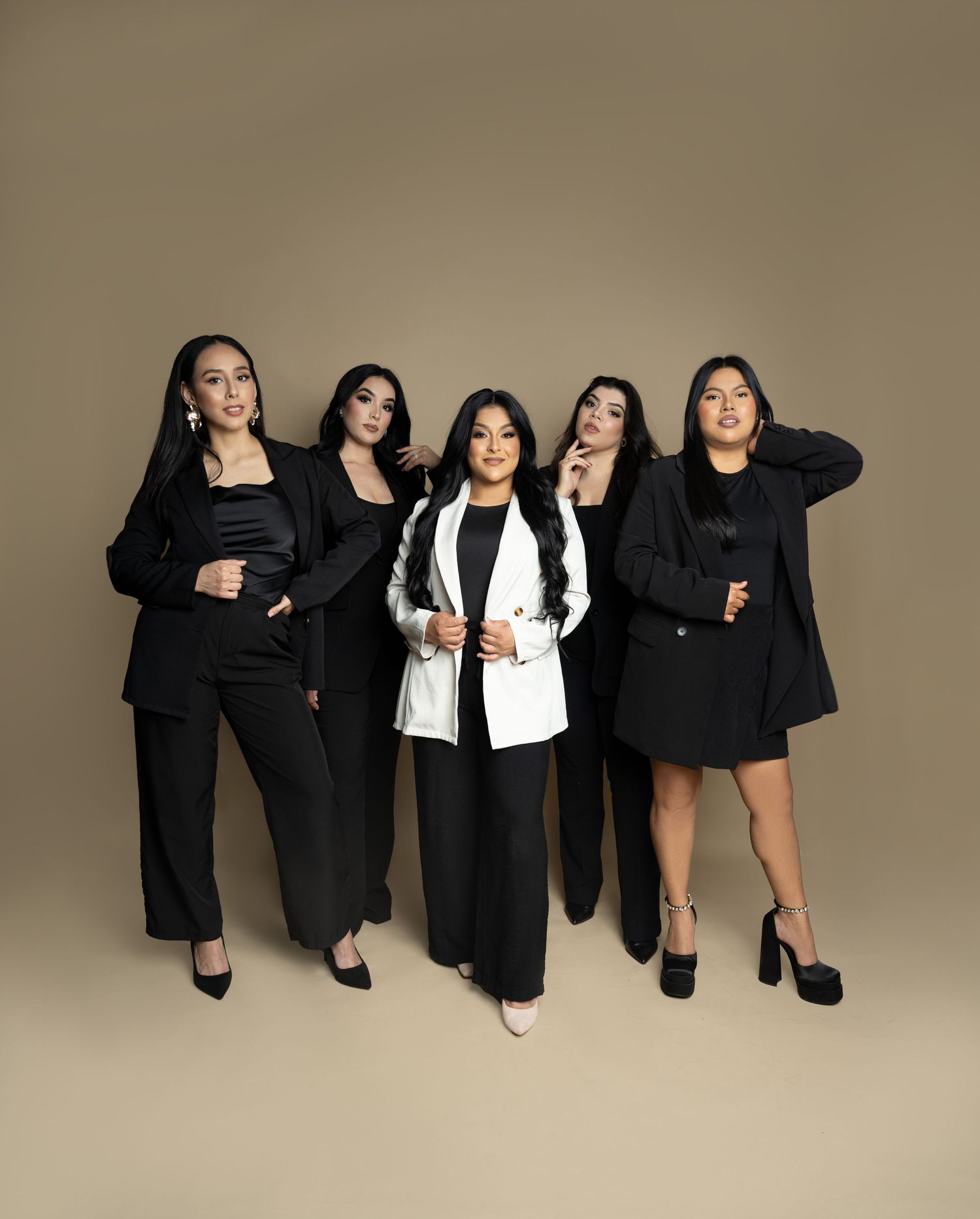 Group of five professionals in black business attire posing together against brown background.