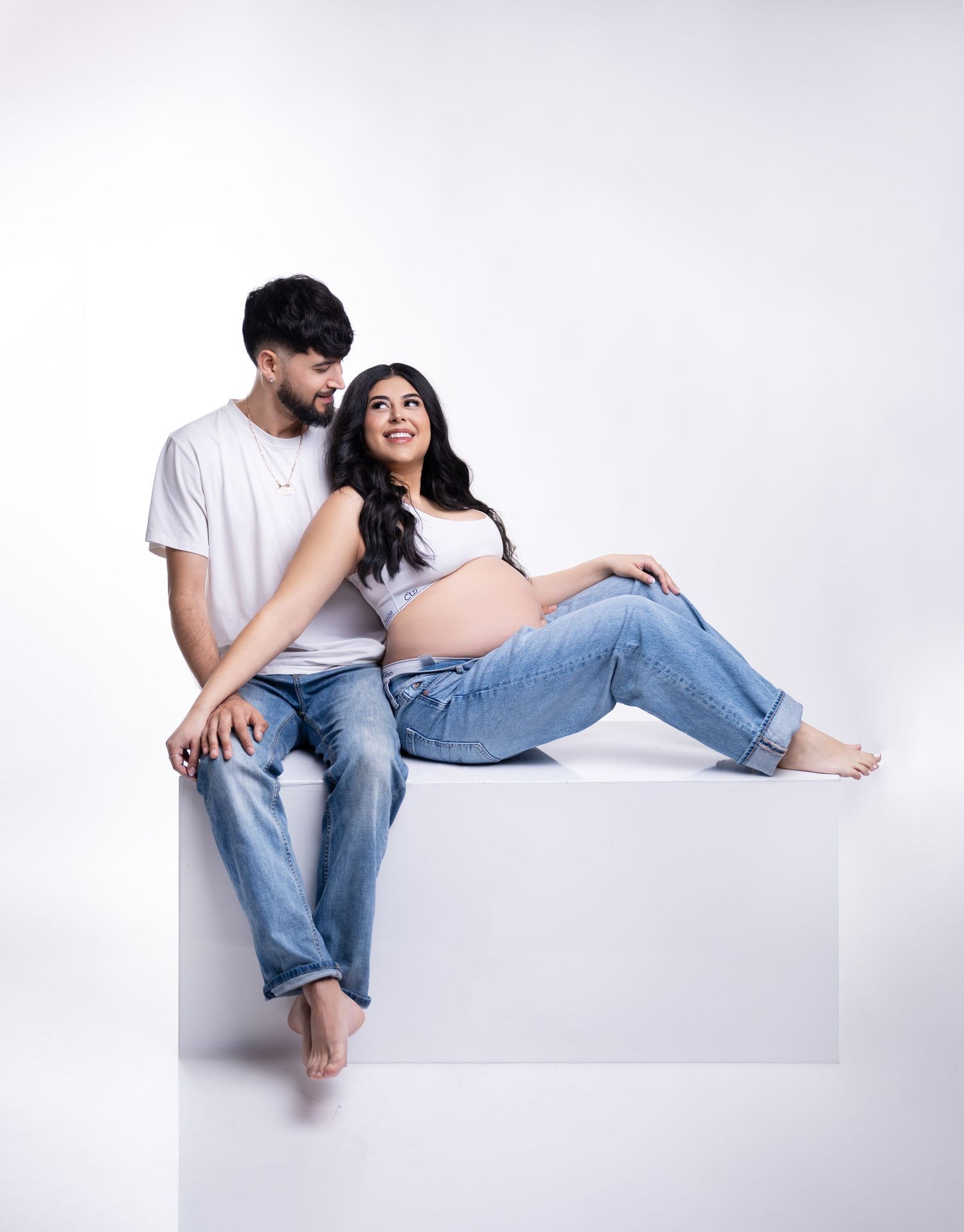 Casual maternity portrait with couple in denim and white sitting on cube.