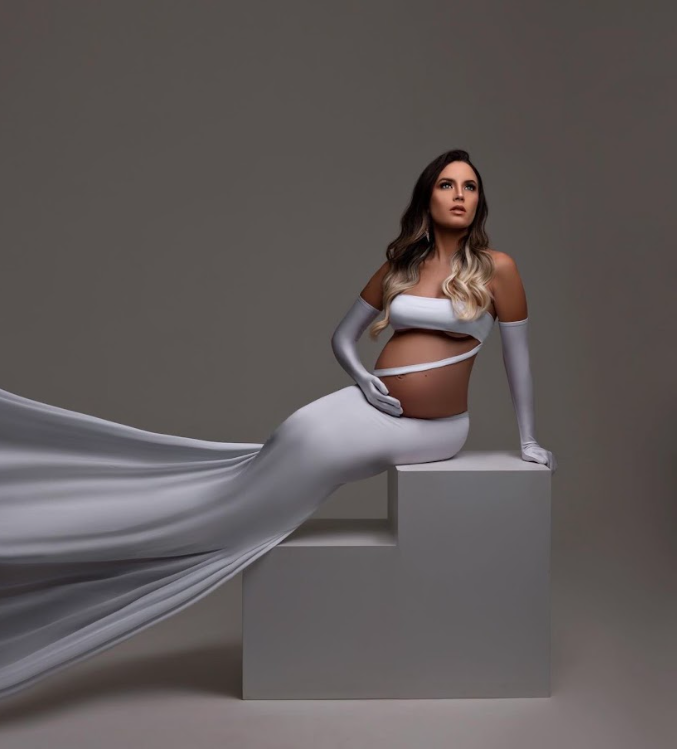 Minimalist maternity photos with flowing white fabric and geometric platforms in studio setting.